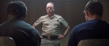 Movie still from “Joy Ride” (2001), directed by John Dahl – A man in a sheriff's uniform stands with his hands on his hips; Medium shot, Low angle