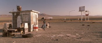 Movie still from “Joy Ride” (2001), directed by John Dahl – A man walking on a dirt road near a building; Extreme Wide shot, Low angle