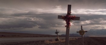 Movie still from “Joy Ride” (2001), directed by John Dahl – A wooden cross with flowers on top of it near a road; Wide shot, Low angle