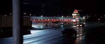 Movie still from “Joy Ride” (2001), directed by John Dahl – A car driving down a street at night past a building; Extreme Wide shot, High angle