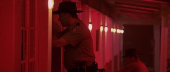 Movie still from “Joy Ride” (2001), directed by John Dahl – A police officer leaning against a wall in a dark room; Medium shot, Low angle