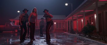 Movie still from “Joy Ride” (2001), directed by John Dahl – A police officer taking a picture of two women in the dark; Wide shot, Low angle