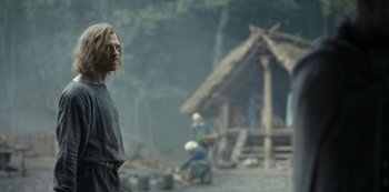Movie still from “Barbarians” (2020), created by Arne Nolting – A man standing in front of a hut in a forest; Medium shot, Over the shoulder angle