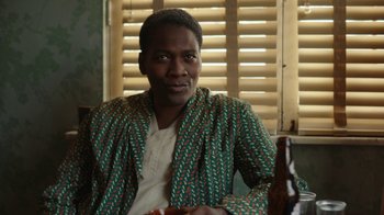 Movie still from “A League of Their Own” (2022), created by Abbi Jacobson – A man sitting in front of a window holding a beer; Close Up shot, Over the shoulder angle