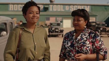 Movie still from “A League of Their Own” (2022), created by Abbi Jacobson – Two women standing next to each other in front of a building; Medium shot, Over the shoulder angle