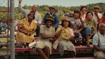Movie still from “A League of Their Own” (2022), created by Abbi Jacobson – A group of people sitting on top of a red bench; Medium shot, Low angle