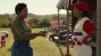 Movie still from “A League of Their Own” (2022), created by Abbi Jacobson – Two women are exchanging cards at a baseball game; Medium shot, Over the shoulder angle