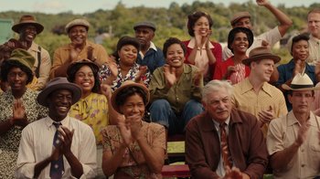Movie still from “A League of Their Own” (2022), created by Abbi Jacobson – A group of men and women clapping in front of trees; Medium shot, Over the shoulder angle