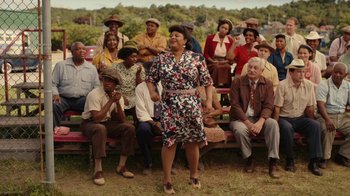 Movie still from “A League of Their Own” (2022), created by Abbi Jacobson – An older woman standing in front of a group of people; Wide shot, Over the shoulder angle