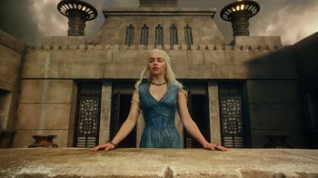 Movie still from “Game of Thrones” (2011), created by D.B. Weiss – Daenerys targaryen is standing in front of a building; Wide shot, Low angle