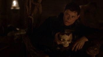 Movie still from “Game of Thrones” (2011), created by D.B. Weiss – A young man holding a skull in a dark room; Close Up shot, Low angle