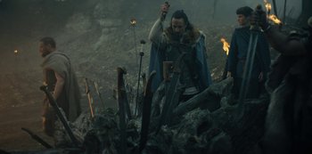 Movie still from “Barbarians” (2020), created by Arne Nolting – A man with a sword standing on a pile of wood; Medium shot, Low angle