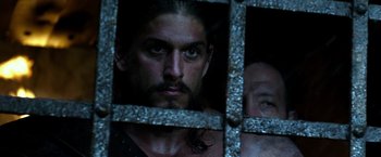 Movie still from “Pompeii” (2014), directed by Paul W.S. Anderson – A person behind a metal fence; Close Up shot, Over the shoulder angle