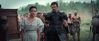 Movie still from “Pompeii” (2014), directed by Paul W.S. Anderson – A man and a woman in roman garb in front of a group of people; Medium shot, Over the shoulder angle