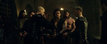 Movie still from “Pompeii” (2014), directed by Paul W.S. Anderson – A group of men standing next to each other in a room; Medium shot, Over the shoulder angle