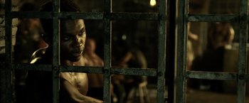 Movie still from “Pompeii” (2014), directed by Paul W.S. Anderson – A man standing in a room behind a metal fence; Close Up shot, Over the shoulder angle