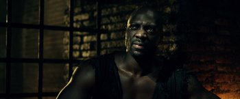 Movie still from “Pompeii” (2014), directed by Paul W.S. Anderson – A man in a black shirt is looking at the camera; Close Up shot, Low angle