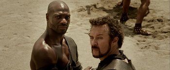 Movie still from “Pompeii” (2014), directed by Paul W.S. Anderson – Two men standing next to each other on a beach; Close Up shot, Over the shoulder angle
