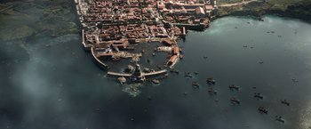 Movie still from “Pompeii” (2014), directed by Paul W.S. Anderson – An aerial view of a city with boats in the water; Extreme Wide shot, High angle