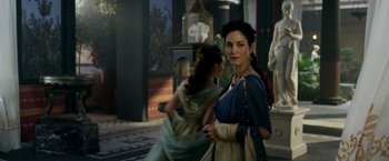 Movie still from “Pompeii” (2014), directed by Paul W.S. Anderson – A woman in a blue and white dress standing in front of two other women; Medium shot, Over the shoulder angle