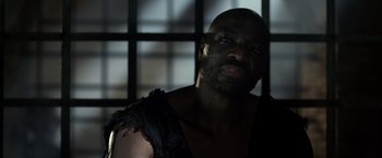 Movie still from “Pompeii” (2014), directed by Paul W.S. Anderson – A man in a black shirt is looking at the camera; Close Up shot, Low angle