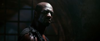 Movie still from “Pompeii” (2014), directed by Paul W.S. Anderson – A man with a beard is standing in a dark room; Close Up shot, Low angle