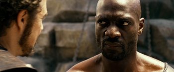 Movie still from “Pompeii” (2014), directed by Paul W.S. Anderson – A man's face with a chain around his neck; Close Up shot, Over the shoulder angle