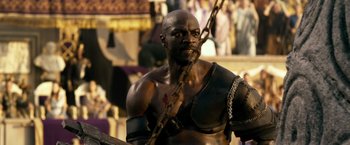 Movie still from “Pompeii” (2014), directed by Paul W.S. Anderson – A man with a chain around his neck and chest; Medium shot, Low angle