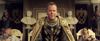 Movie still from “Pompeii” (2014), directed by Paul W.S. Anderson – A man wearing a suit of armor in front of statues of busts; Close Up shot, Over the shoulder angle