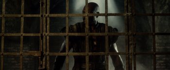 Movie still from “Pompeii” (2014), directed by Paul W.S. Anderson – A man in chains looking out of a jail cell; Medium shot, Low angle