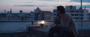 Movie still from “Berlin Syndrome” (2017), directed by Cate Shortland – A man sitting on top of a building at night; Medium shot, Low angle
