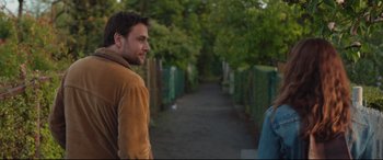 Movie still from “Berlin Syndrome” (2017), directed by Cate Shortland – A young man standing on a sidewalk next to trees; Close Up shot, Over the shoulder angle