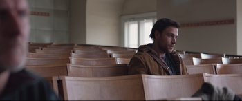 Movie still from “Berlin Syndrome” (2017), directed by Cate Shortland – A man sitting alone in a room with many wooden chairs; Medium shot, Over the shoulder angle
