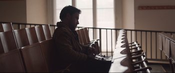 Movie still from “Berlin Syndrome” (2017), directed by Cate Shortland – A man sitting at a table in a room; Medium shot, High angle