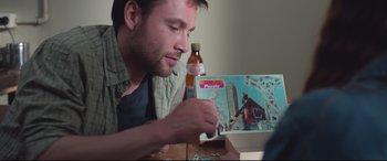 Movie still from “Berlin Syndrome” (2017), directed by Cate Shortland – A man is holding a bottle and looking at a puzzle; Close Up shot, Over the shoulder angle