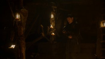 Movie still from “Game of Thrones” (2011), created by D.B. Weiss – A man standing next to a candle in a dark room; Medium shot, High angle
