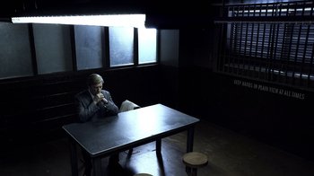 Movie still from “Better Call Saul” (2015), created by Vince Gilligan – A man sitting at a table in a dark room; Wide shot, High angle