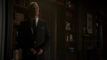 Movie still from “Better Call Saul” (2015), created by Vince Gilligan – A man in a suit and tie standing in front of a book case; Medium shot, Low angle