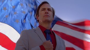 Movie still from “Better Call Saul” (2015), created by Vince Gilligan – A man in a suit and tie standing in front of an american flag; Close Up shot, Low angle