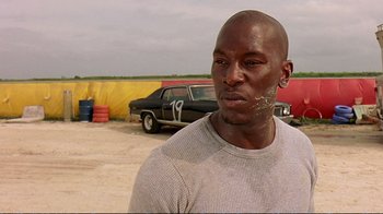 Movie still from “2 Fast 2 Furious” (2003), directed by John Singleton – A man standing in front of a car in a parking lot; Close Up shot, Low angle