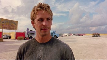 Movie still from “2 Fast 2 Furious” (2003), directed by John Singleton – A person wearing a t - shirt near a parking lot; Close Up shot, Over the shoulder angle