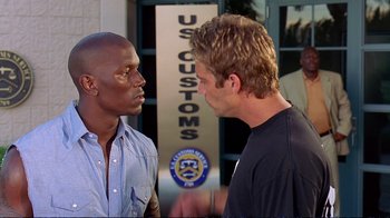 Movie still from “2 Fast 2 Furious” (2003), directed by John Singleton – Two men talking to each other in front of a us customs building; Medium shot, Over the shoulder angle