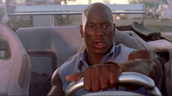Movie still from “2 Fast 2 Furious” (2003), directed by John Singleton – A person sitting in a car holding a steering wheel; Close Up shot, Low angle