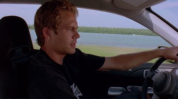 Movie still from “2 Fast 2 Furious” (2003), directed by John Singleton – A man driving a car on a road near a body of water; Close Up shot, Over the shoulder angle