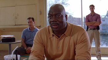 Movie still from “2 Fast 2 Furious” (2003), directed by John Singleton – A man in a tan shirt is sitting in front of another man in a blue shirt; Medium shot, Low angle