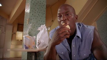 Movie still from “2 Fast 2 Furious” (2003), directed by John Singleton – A man is eating a sandwich in a restaurant; Medium shot, Low angle
