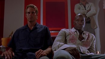 Movie still from “2 Fast 2 Furious” (2003), directed by John Singleton – A couple of men sitting next to each other on top of a couch; Medium shot, Low angle