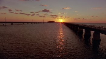 Movie still from “2 Fast 2 Furious” (2003), directed by John Singleton – The sun is setting over the ocean with a bridge in the background; Extreme Wide shot, Low angle