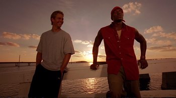 Movie still from “2 Fast 2 Furious” (2003), directed by John Singleton – Two men standing next to a body of water at sunset; Medium shot, Low angle