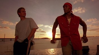 Movie still from “2 Fast 2 Furious” (2003), directed by John Singleton – Two men standing next to a body of water at sunset; Medium shot, Low angle